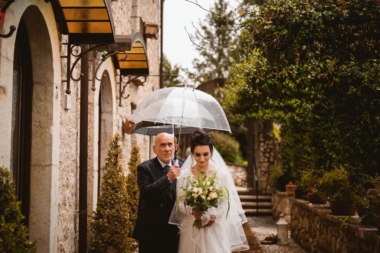 sposa e padre della sposa che camminano con un ombrello in mano