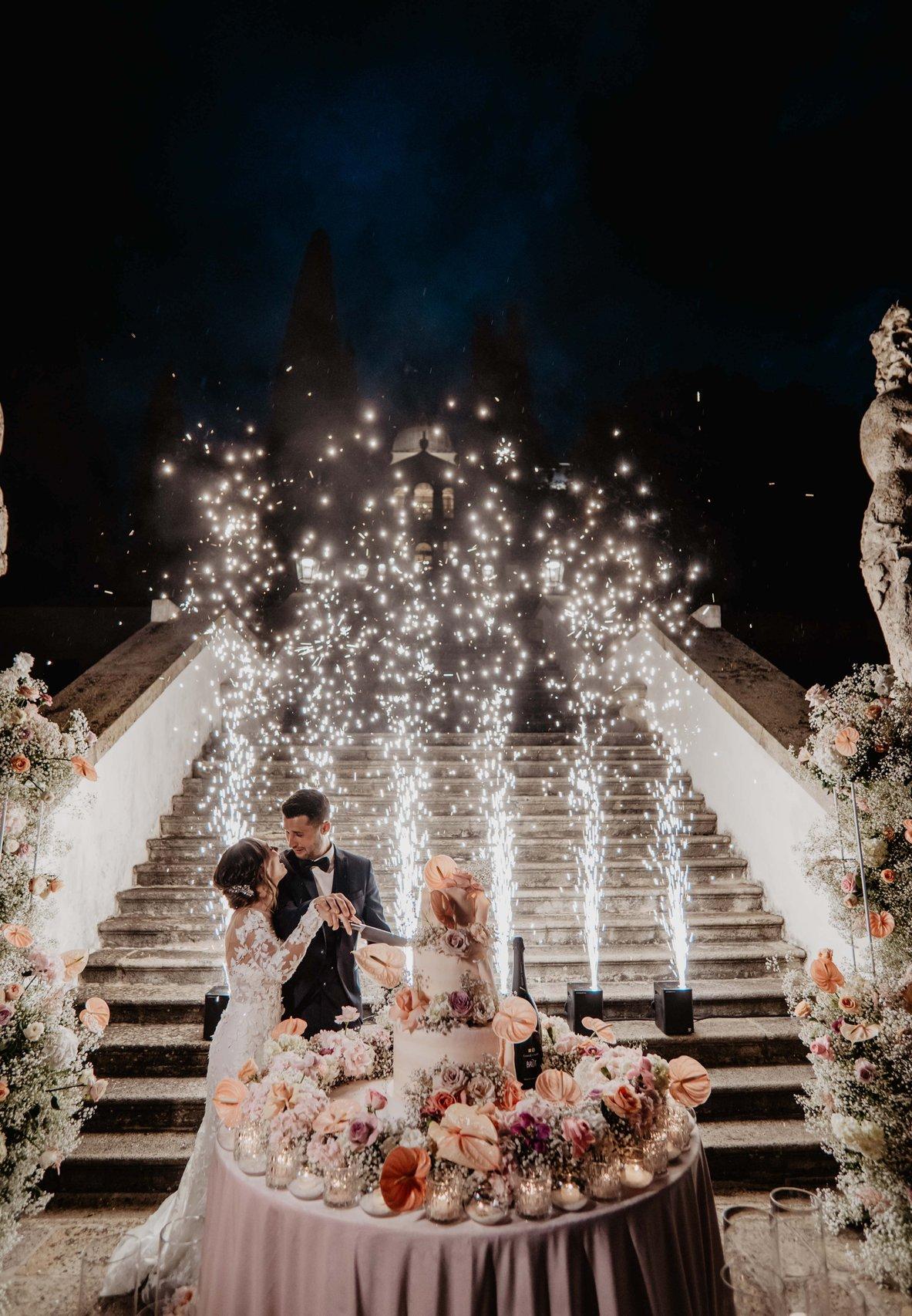 sposi che tagliano la torta con i fuochi d'artificio e decorazioni floreali in stile matrimonio perlage- stili matrimonio