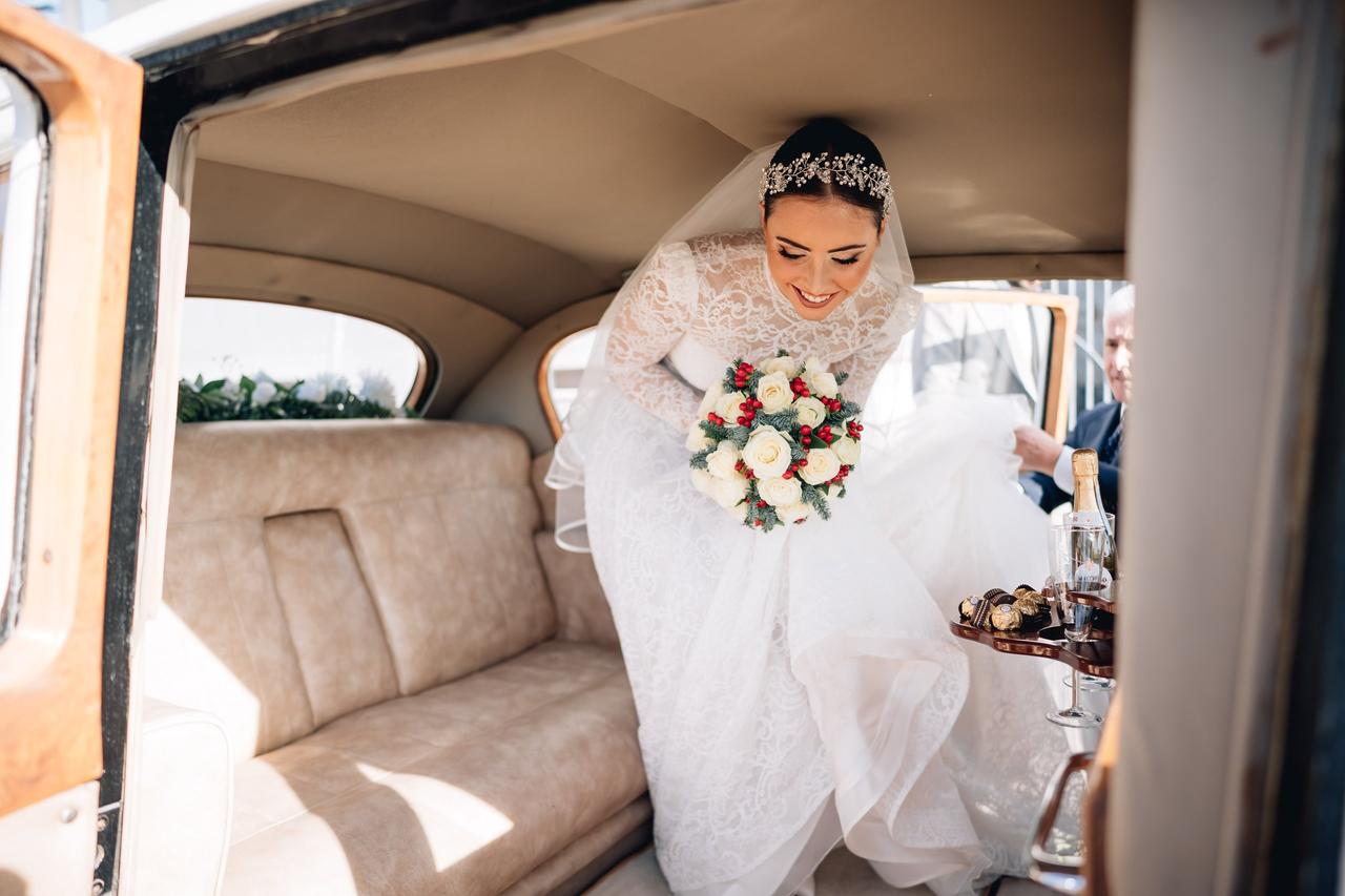 sposa che scende dalla macchina tenendo in mano bouquet sposa invernale con fiori bianchi e bacche rosse