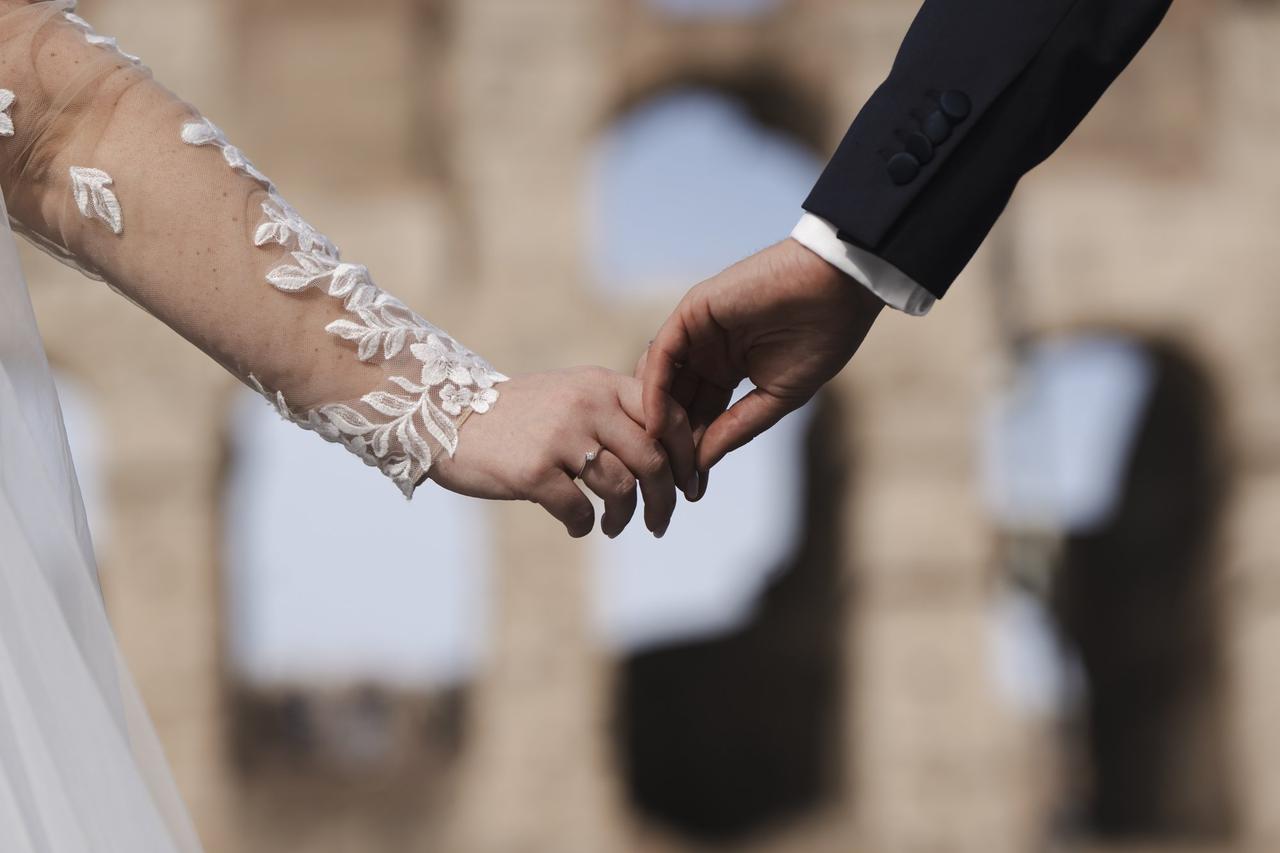 sposi che si tengono per mano, lei indossa un anello di fidanzamento solitario