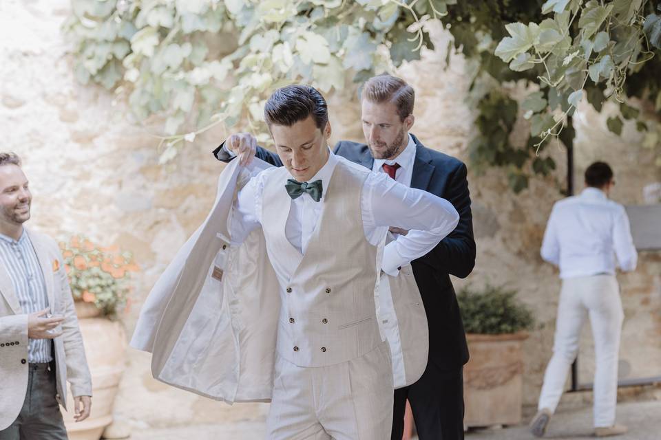 invitato che aiuta sposo a mettersi la giacca del suo abito da sposo beige