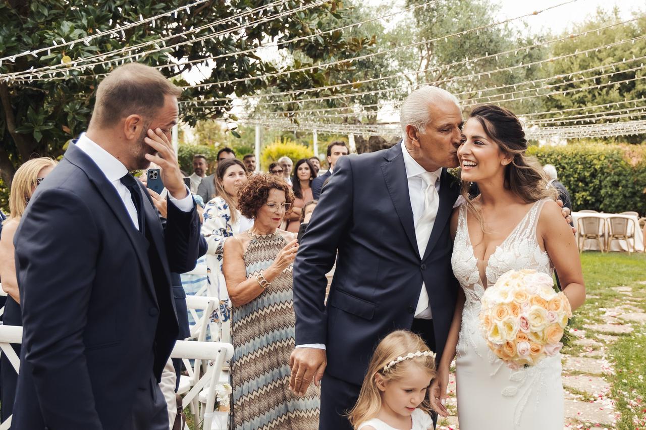padre della sposa che bacia la figlia sulla guancia mentre lo sposi all'altare si emoziona- ordine corteo nuziale