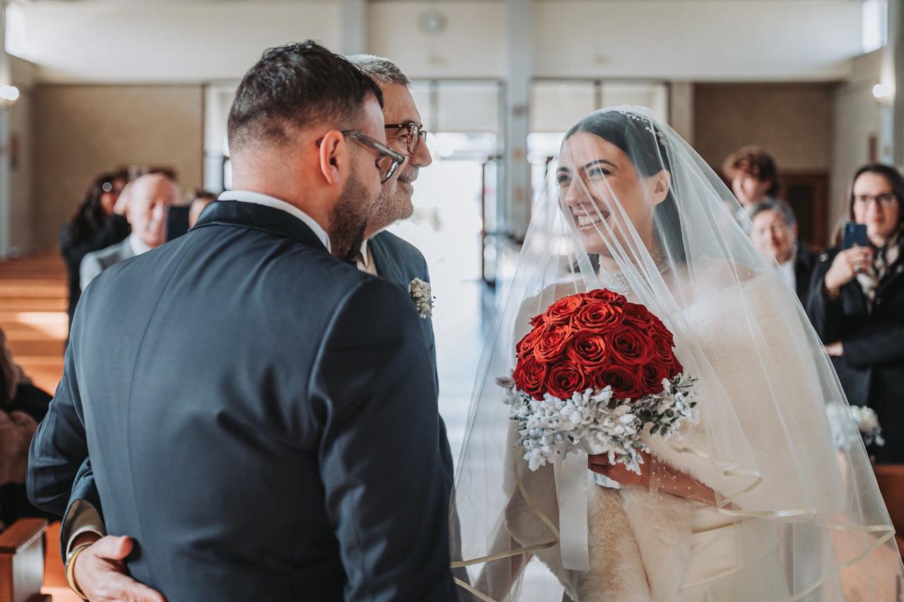 sposa che tiene in mano bouquet da sposa invernale con rose rosse mentre guarda lo sposo negli occhi