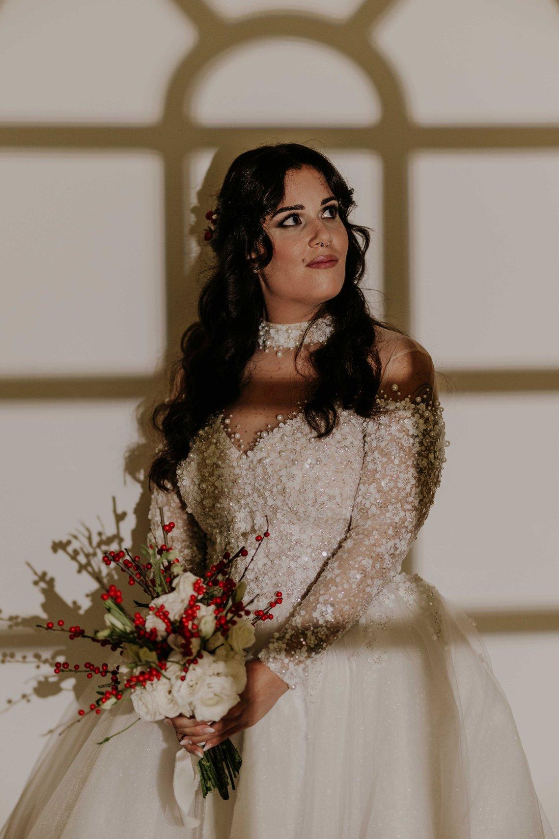 sposa che tiene in mnao bouquet da sposa invernale con fiori bianchi e bacche rosse