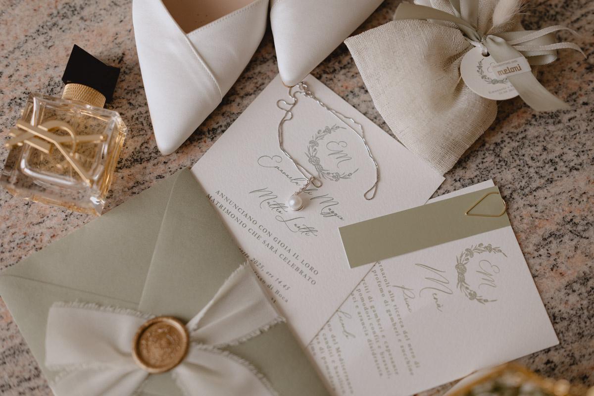 partecipazioni nozze stile boho verdi e bianche, poggiate vicino alle scarpe della sposa, alla bomboniera e al profumo- cosa scrivere sulle partecipazioni di matrimonio
