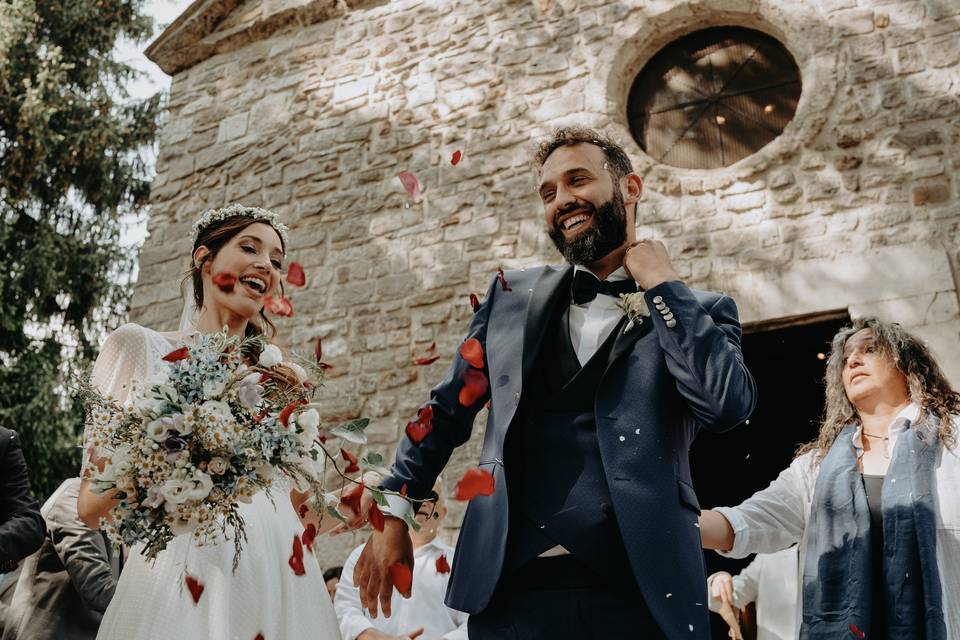sposo e sposa fuori dalla chiesa durante lancio di riso e petali di rosa