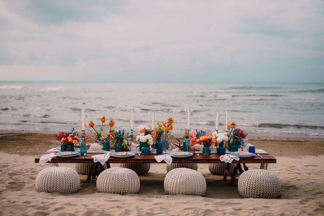 tavolo basso con pouf sulla spiaggia, a pochi metri dal mare, allestito con fiori e candele- sposarsi al mare