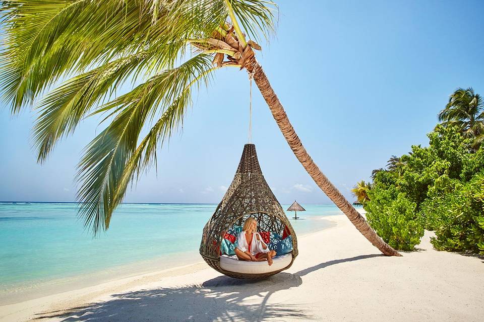 ragazza seduta su una sedia a dondolo in una spiaggia delle Maldive
