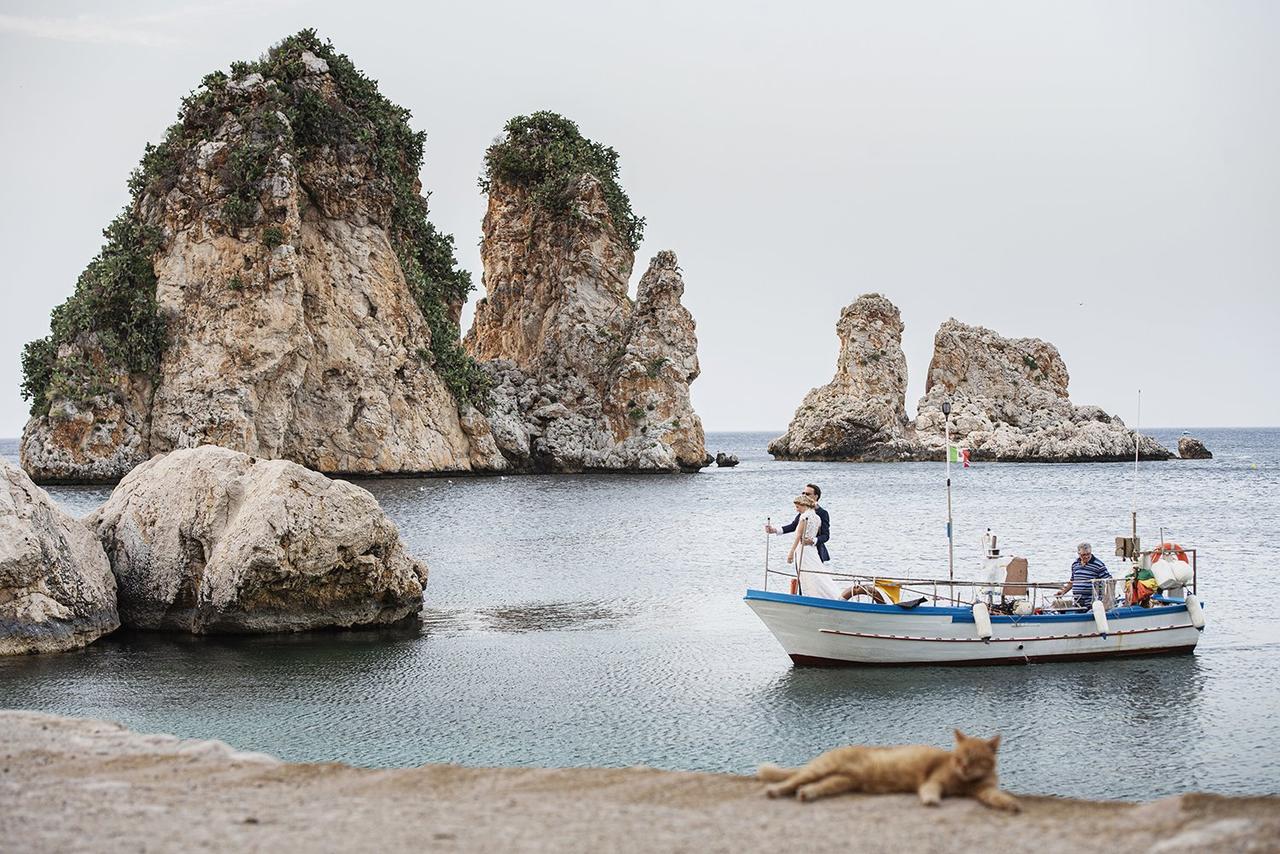 sposi che arrivano ai faraglioni di Scopello in barca per matrimonio stile Mediterraneo