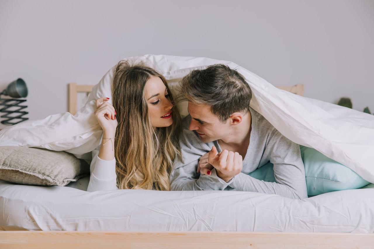 coppia sotto le coperte a letto che si scambia frasi buongiorno