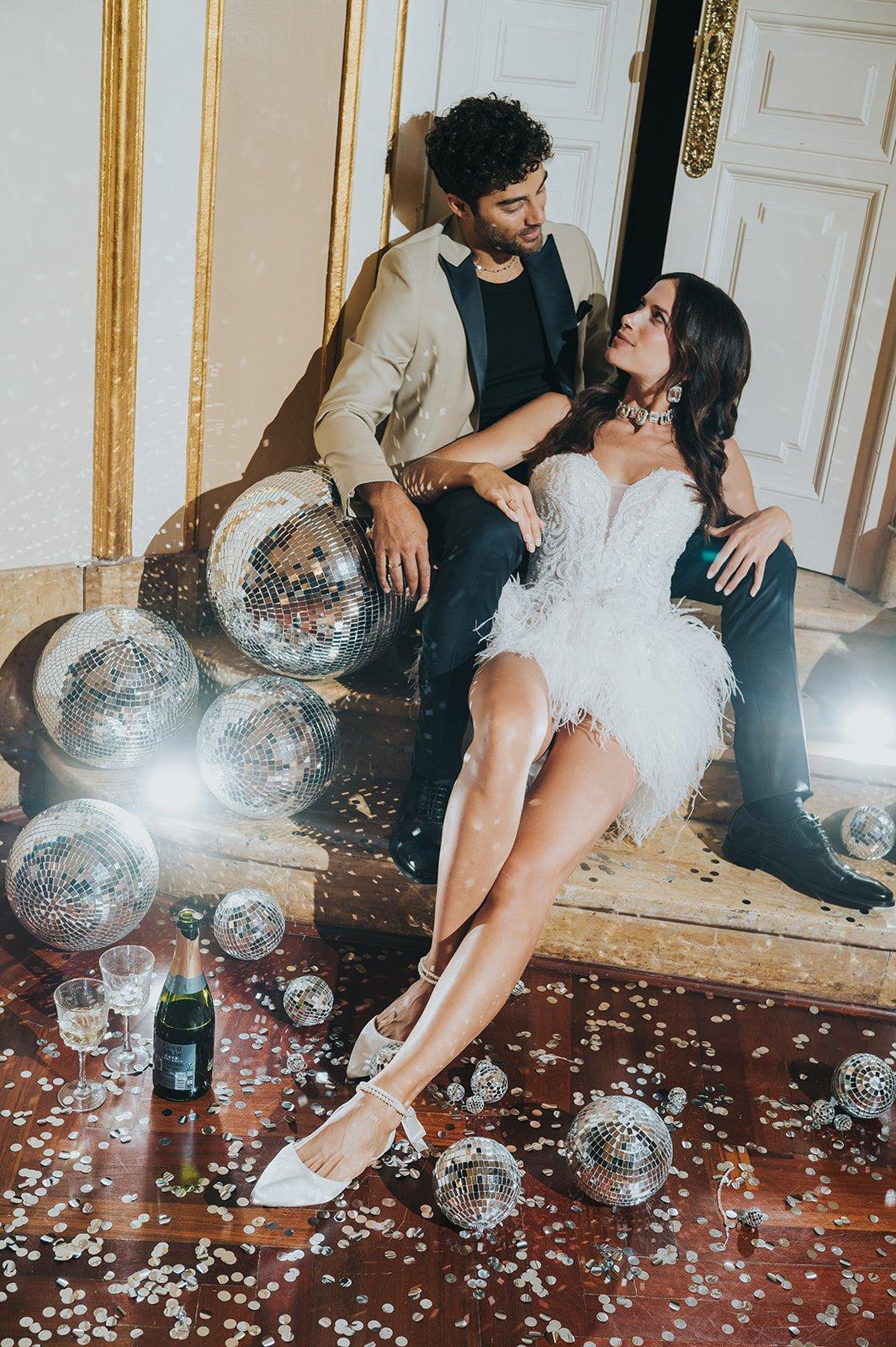 sposi in posa seduti che si guardano in perfetto stile Y2K con deocrazioni anni 200 come disco ball e glitter