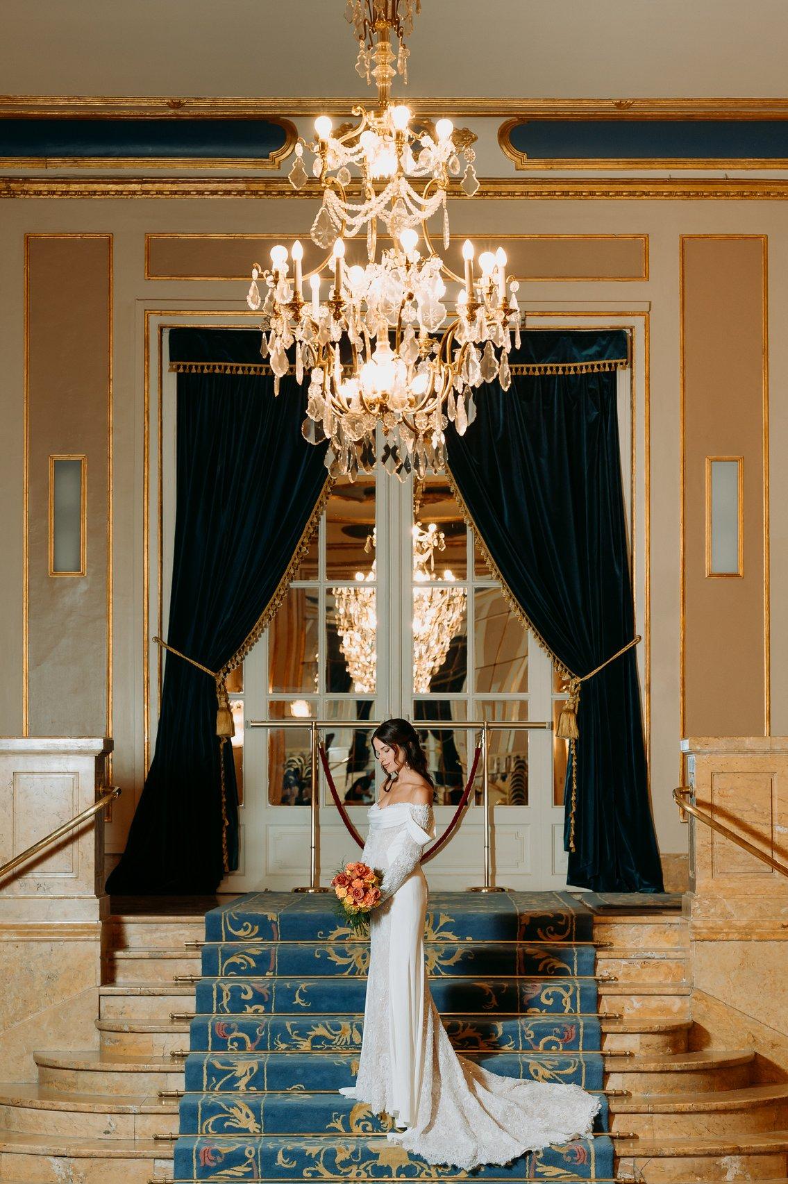sposa in posa all'interno della location in stile Regency, con candelabri in cristallo tende con drappeggi e scalinate con tappeti