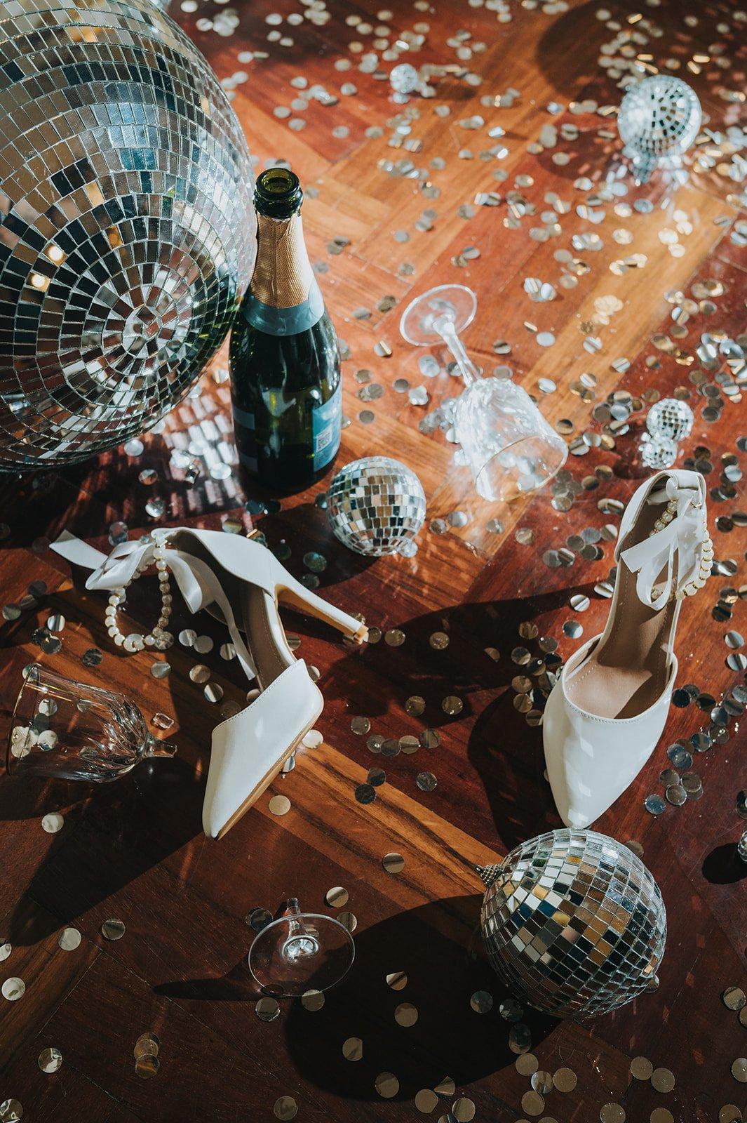 dettagli dell'after party in stile Y2K con bottiglia champagne, scarpe sposa, glitter e disco ball